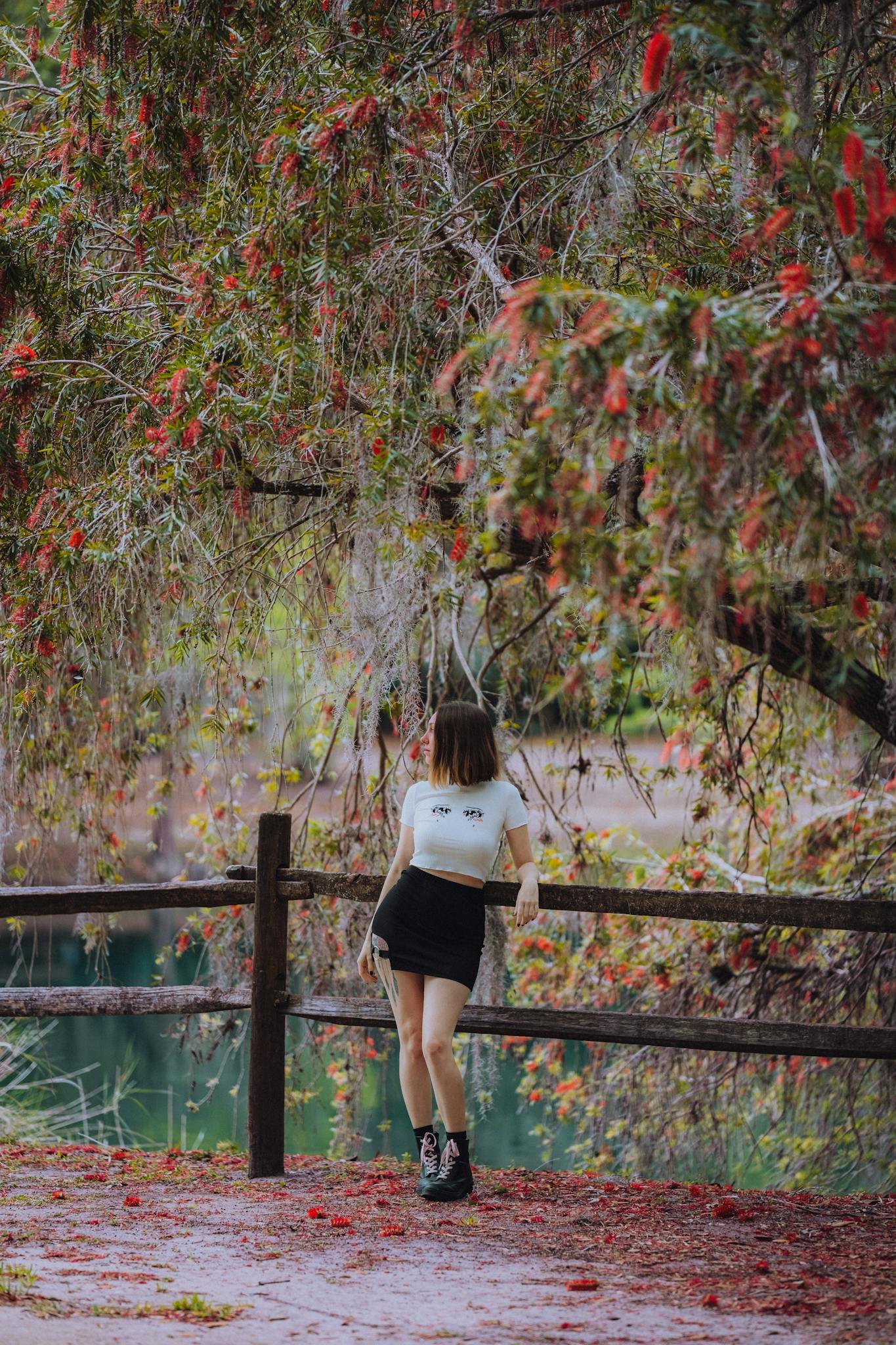 A young woman standing by a wooden fence amidst colorful autumn leaves.